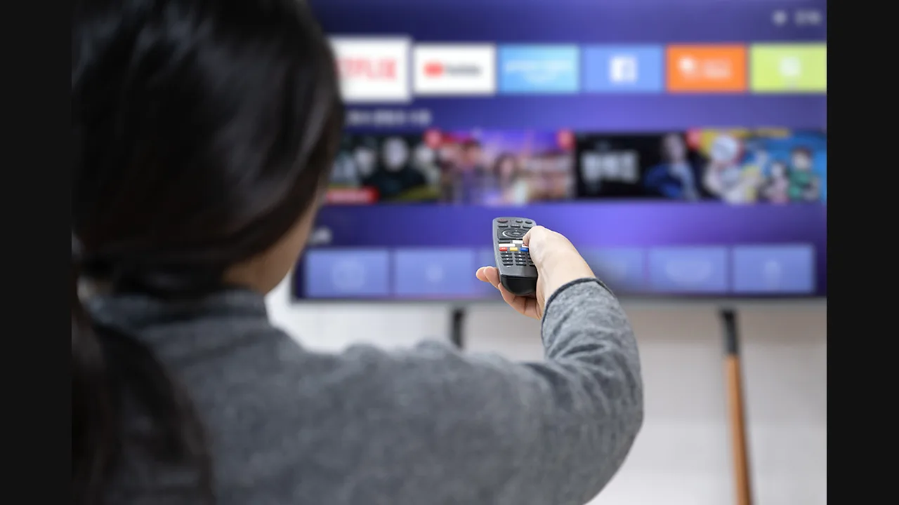 Person holding a remote up to a smart TV showing rows of streaming app icons